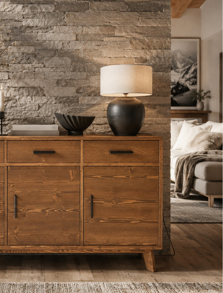 Buffet en bois massif brun foncé dans un intérieur chalet avec mur en pierre, tableau montagne et décoration chaleureuse